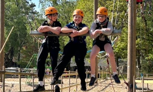 Three students wearing safety hemets raised up in the air on a wooden swing